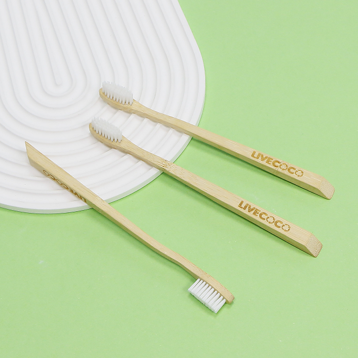 Two bamboo toothbrushes with 'LIVECO' branding on a green background