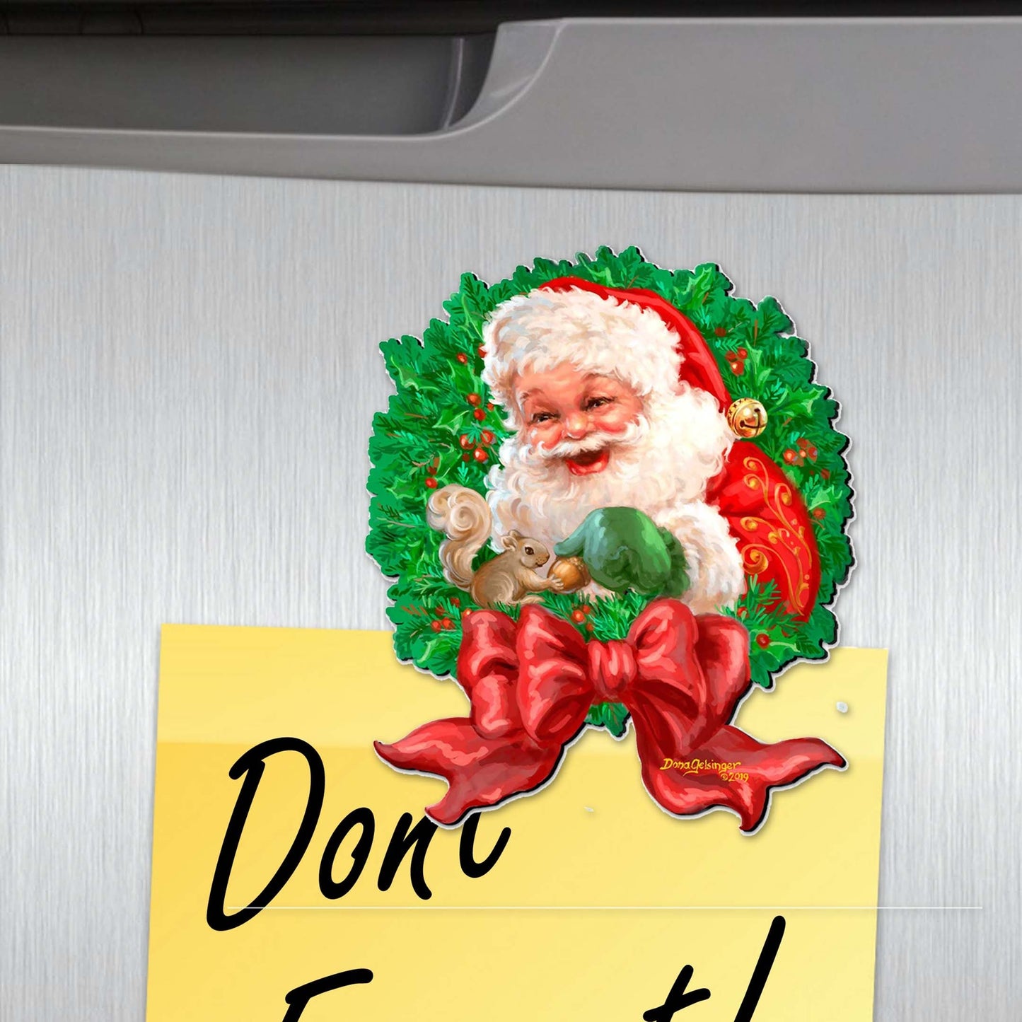 Decorative Christmas magnet with Santa Claus, wreath, and bow on a metallic surface.