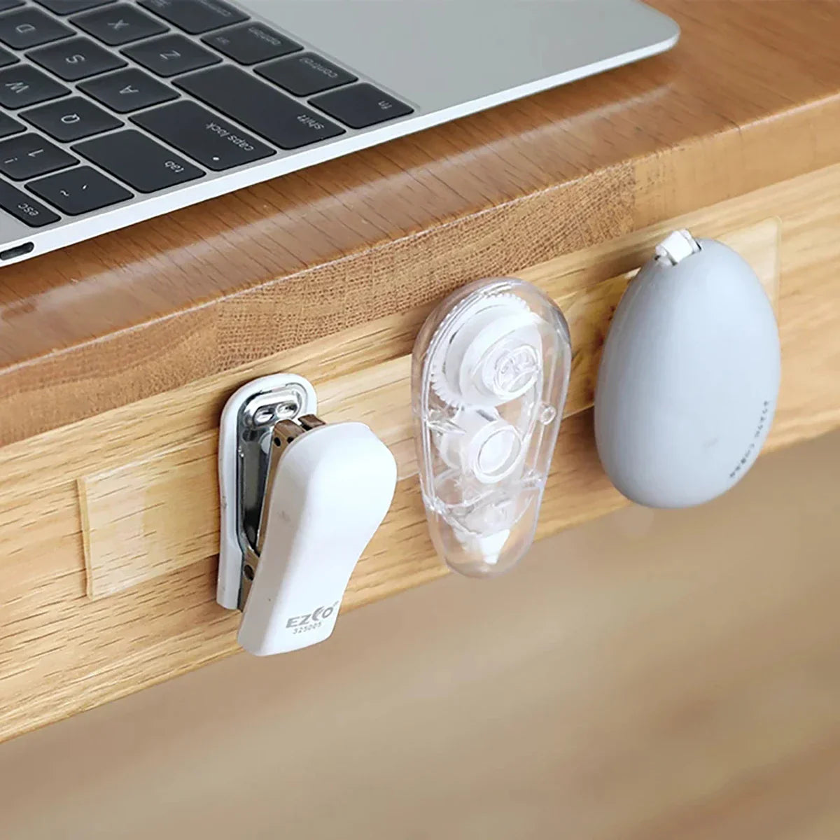 White office supplies including a clip, earbuds, and a small ball on a wooden surface with a laptop.