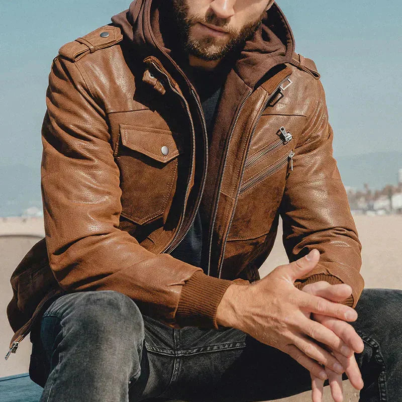 Man wearing a brown leather jacket sitting outdoors with a blurred background