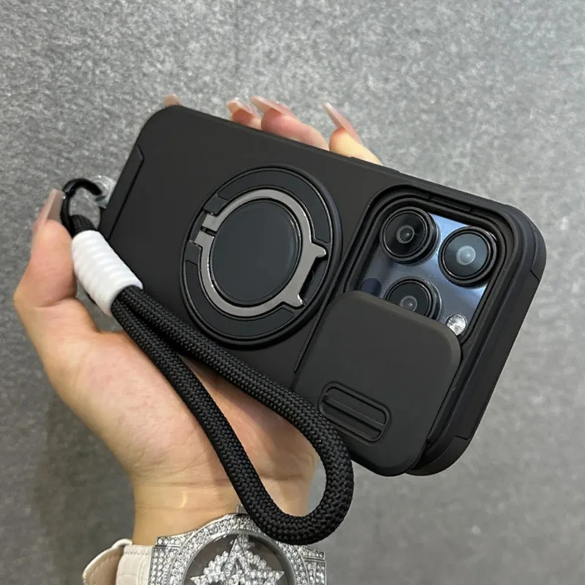 Black phone case with camera lens protector and lanyard held by a hand against a gray background