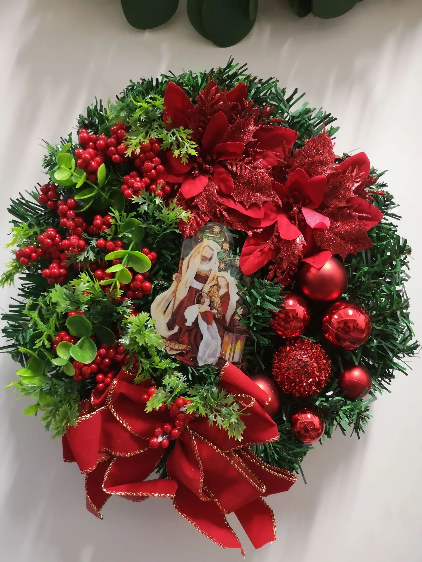 Decorative Christmas wreath with red flowers, berries, and ornaments on a white background