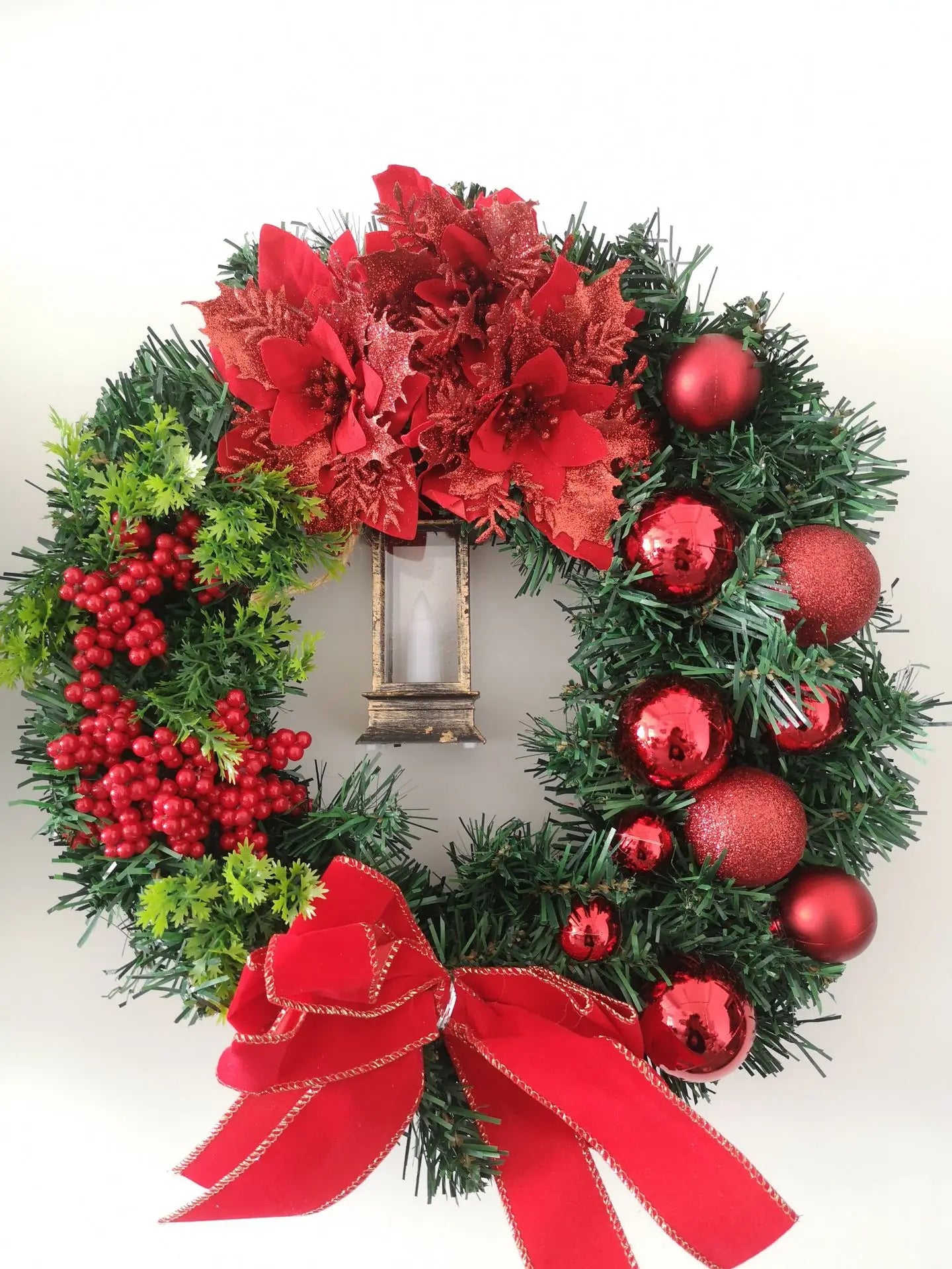 Christmas wreath with red flowers, berries, and ornaments on a white background