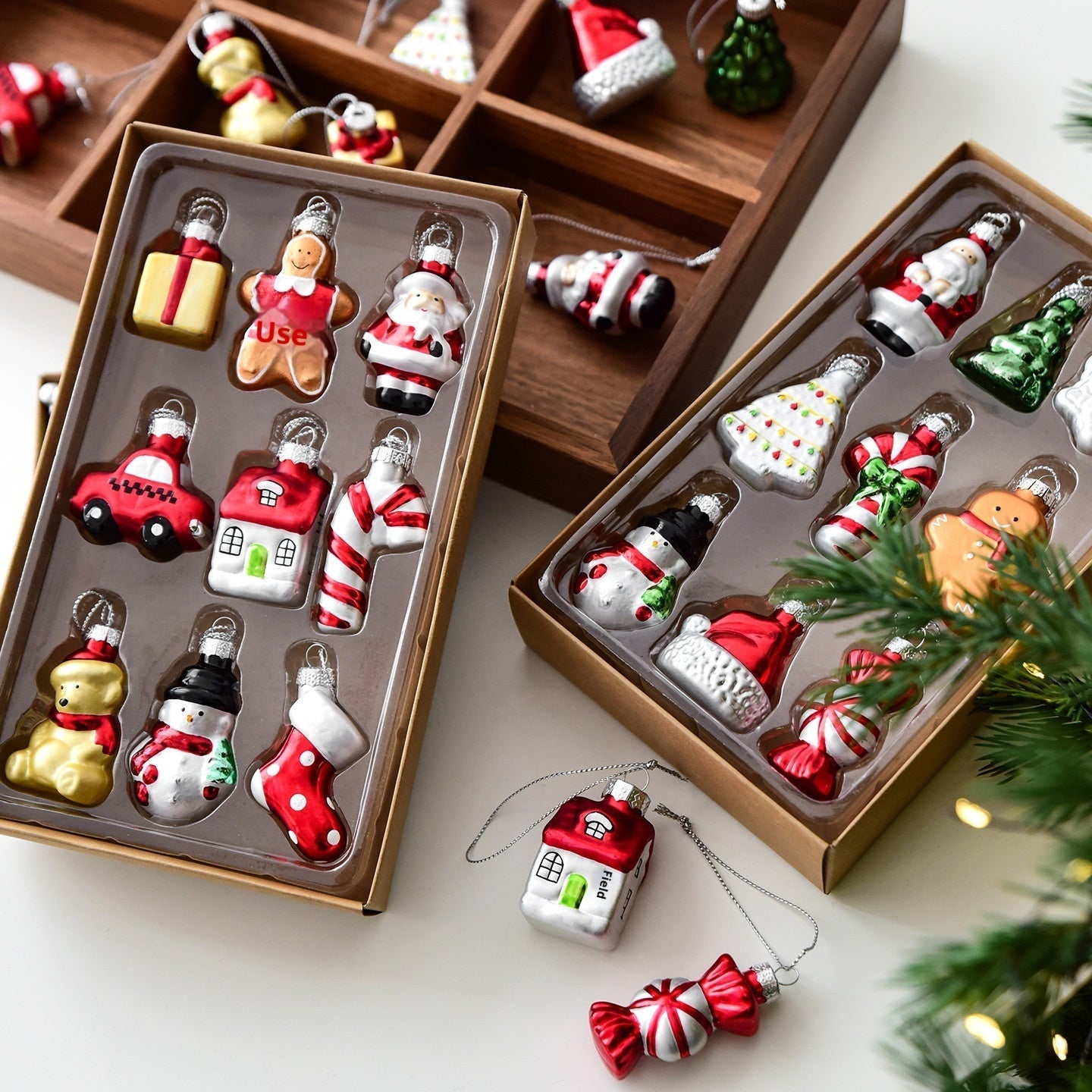 Collection of Christmas-themed miniature ornaments in open boxes on a white surface with a Christmas tree.
