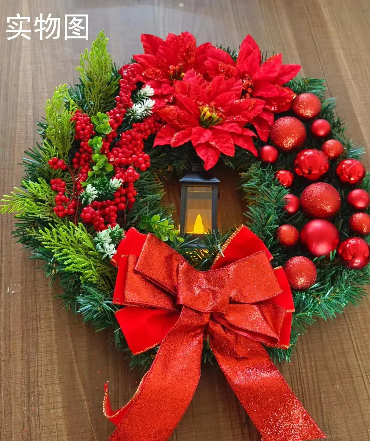 Decorative Christmas wreath with red flowers, berries, and a red bow on a wooden surface.