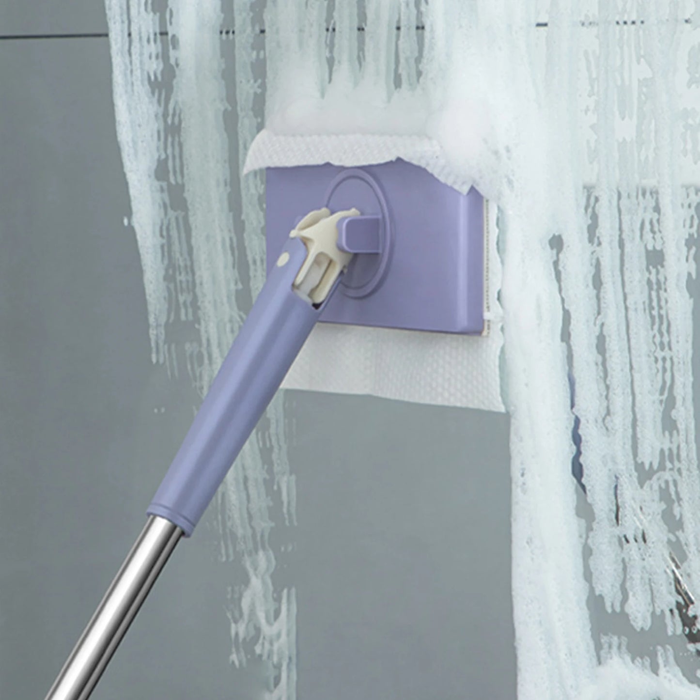 Purple cleaning tool with a spray head against a gray wall with water splashes.