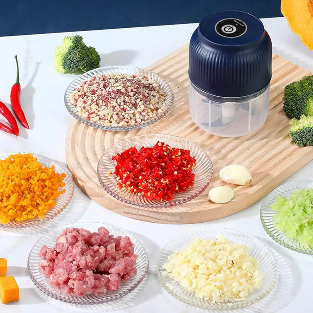Small food processor on a wooden cutting board with various chopped ingredients around it.