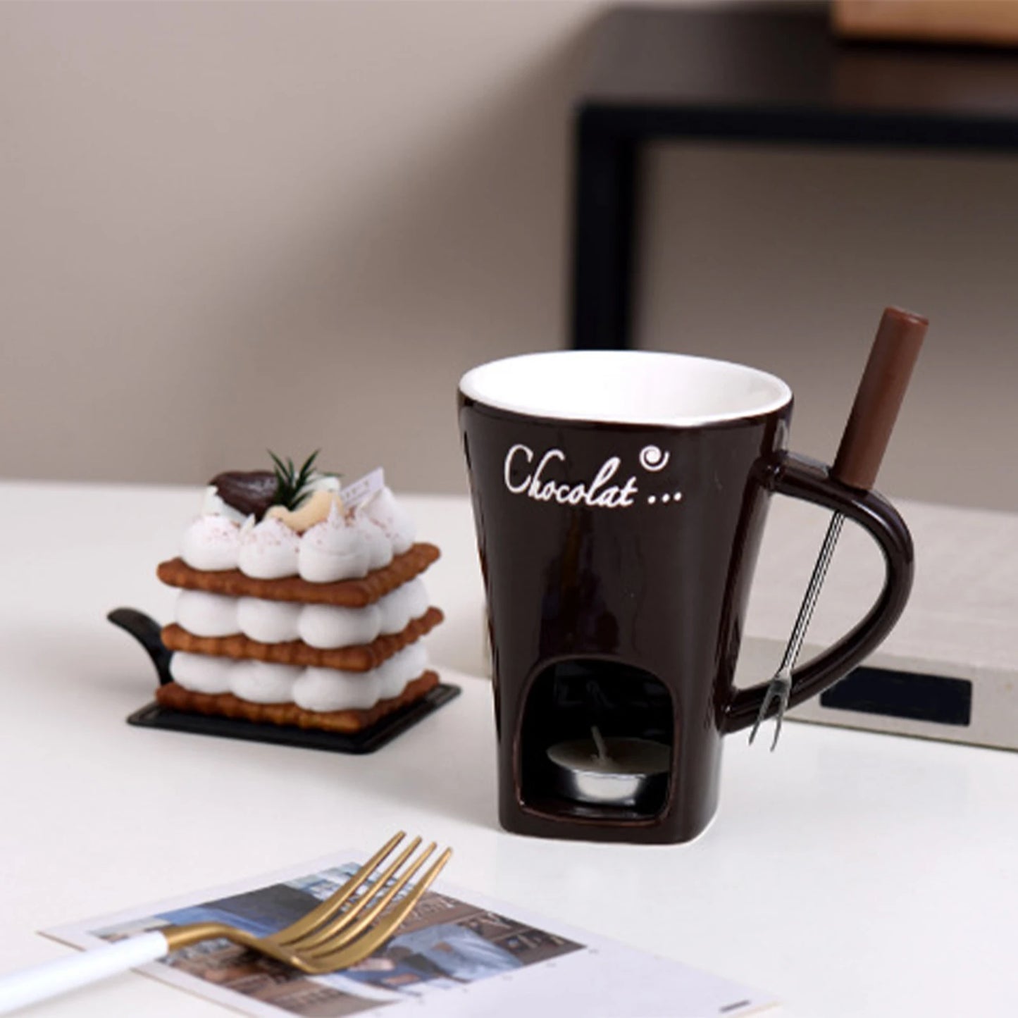 Chocolate-themed mug with a small cake and chocolate bar on a table.
