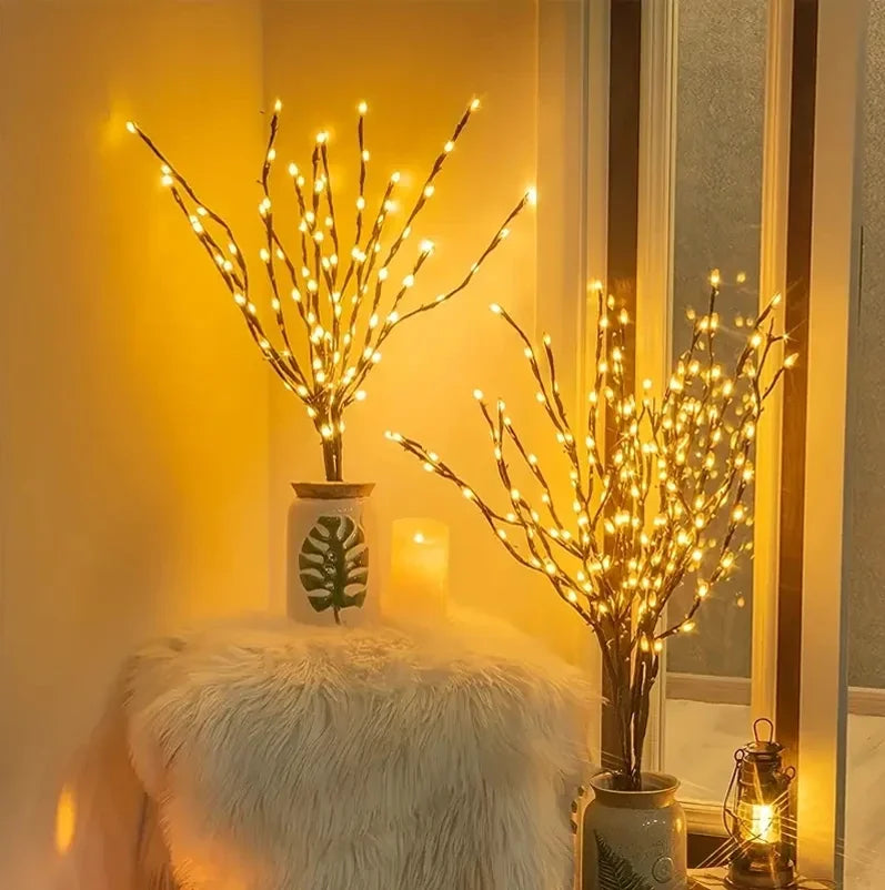 Decorative LED branches with warm lighting on a white surface near a window.
