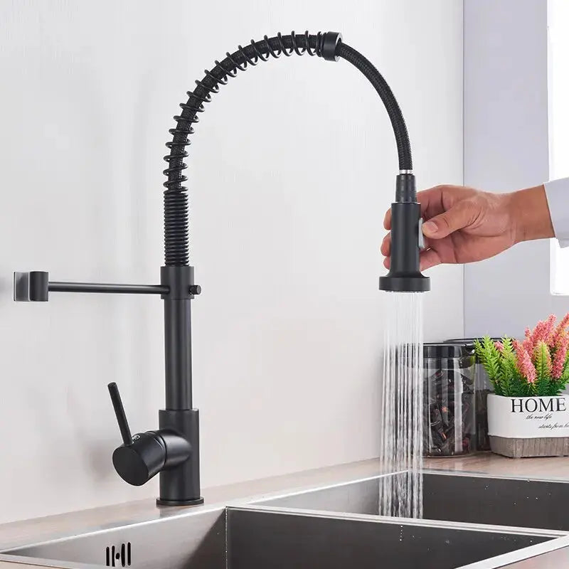 Black kitchen faucet with a hand holding the spray head over a sink.
