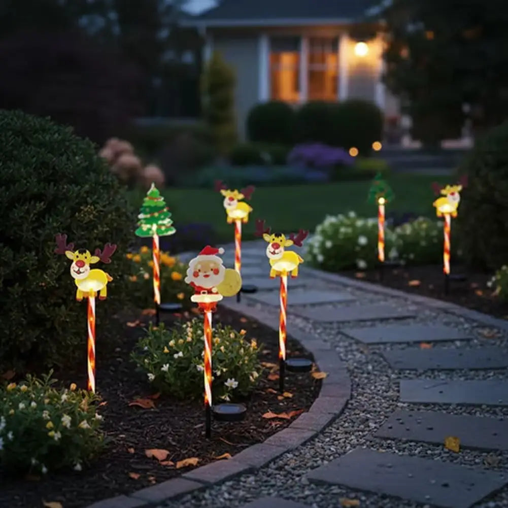 Decorative garden lights shaped like Santa Claus, reindeer, and Christmas trees on a pathway in a garden.