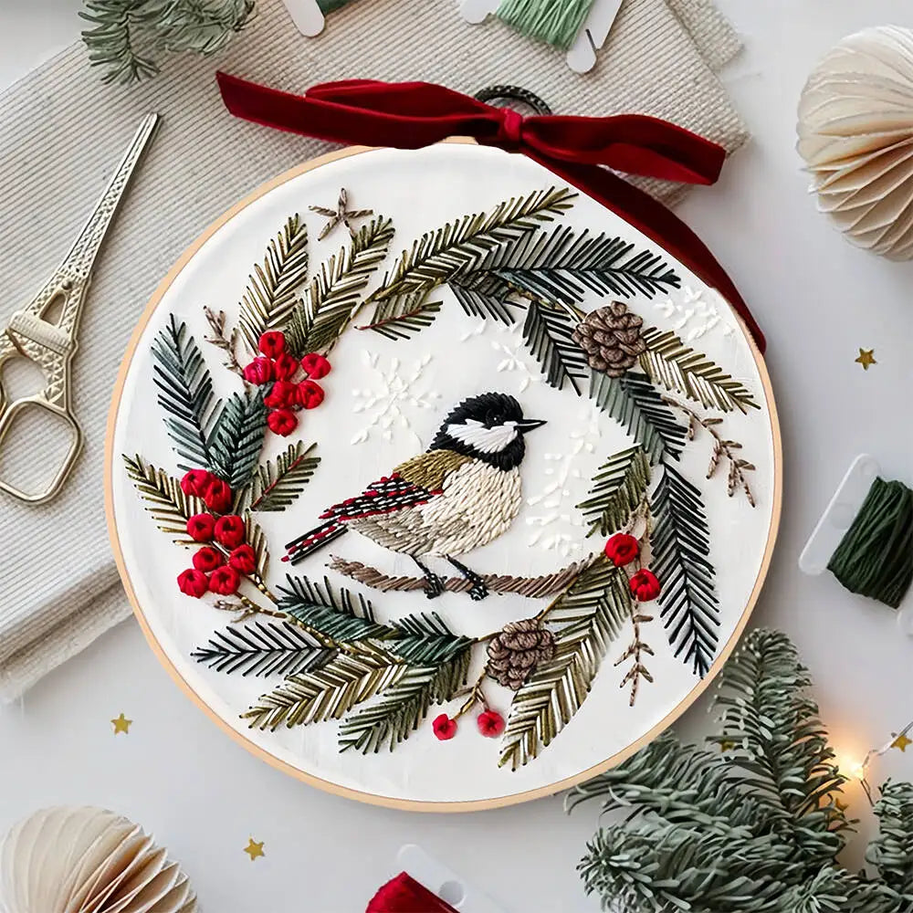 Embroidery hoop with a Christmas-themed design featuring a bird, berries, and evergreen branches.