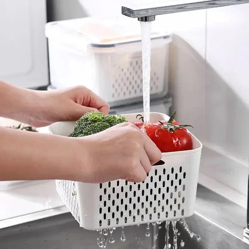 Person washing vegetables in a white perforated basket under running water in a kitchen sink.