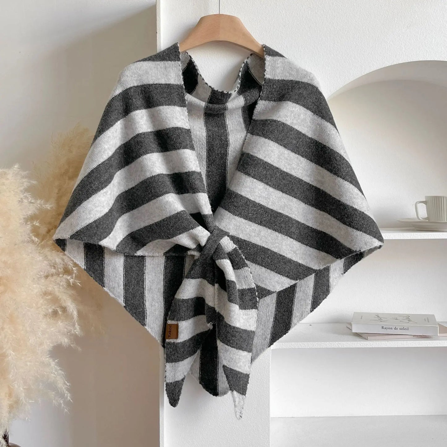 Black and white striped poncho on a wooden hanger against a neutral background
