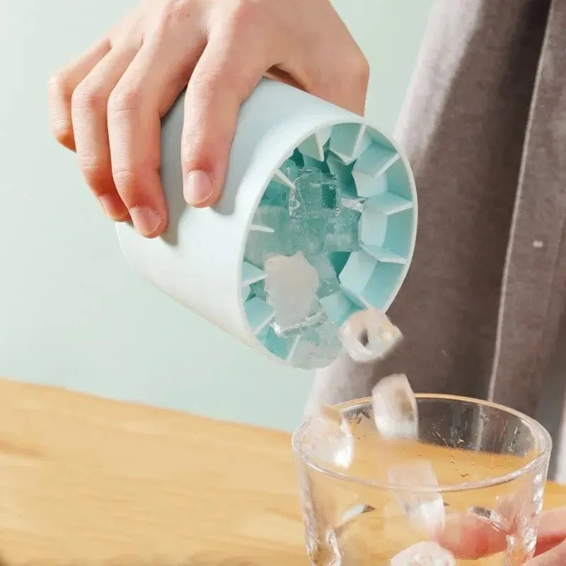 Hand using a ice cube tray to pour ice cubes into a glass on a wooden surface.
