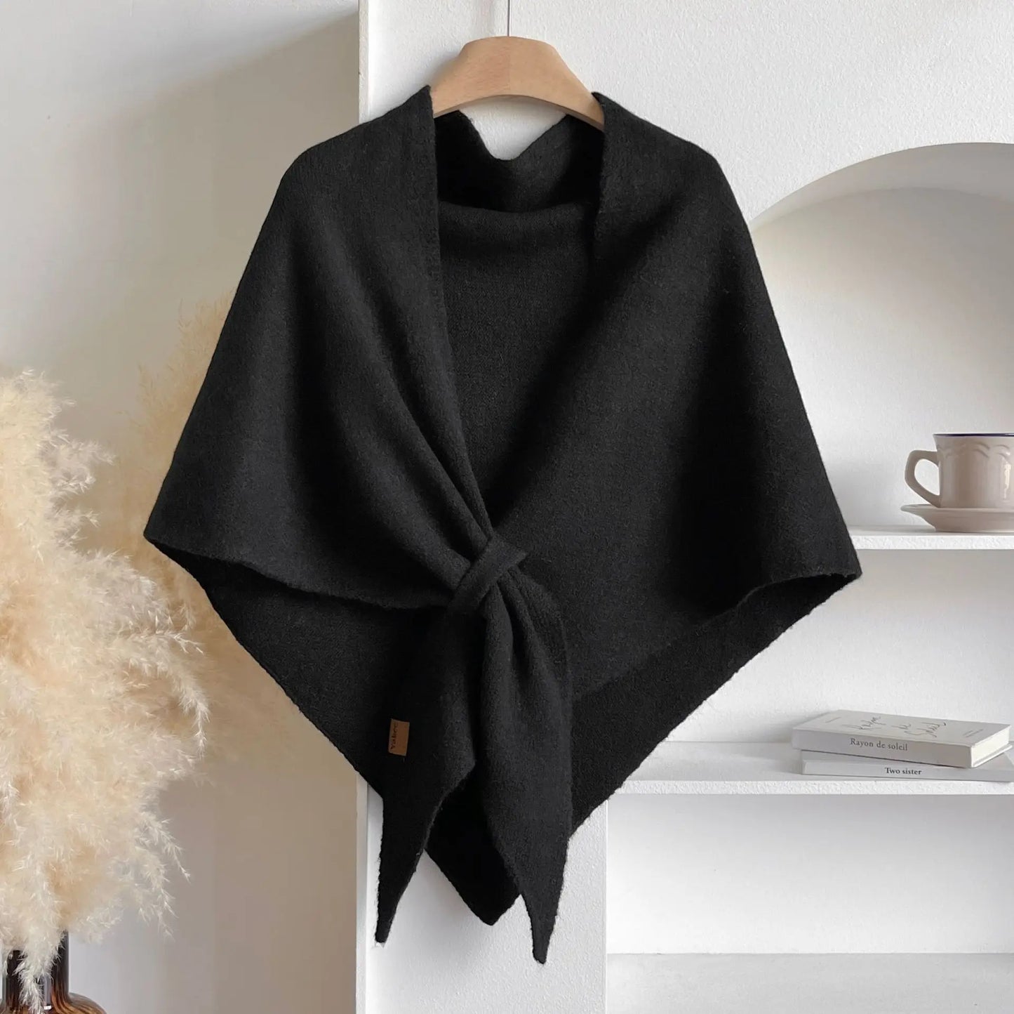Black poncho on a hanger against a white wall with decor elements.