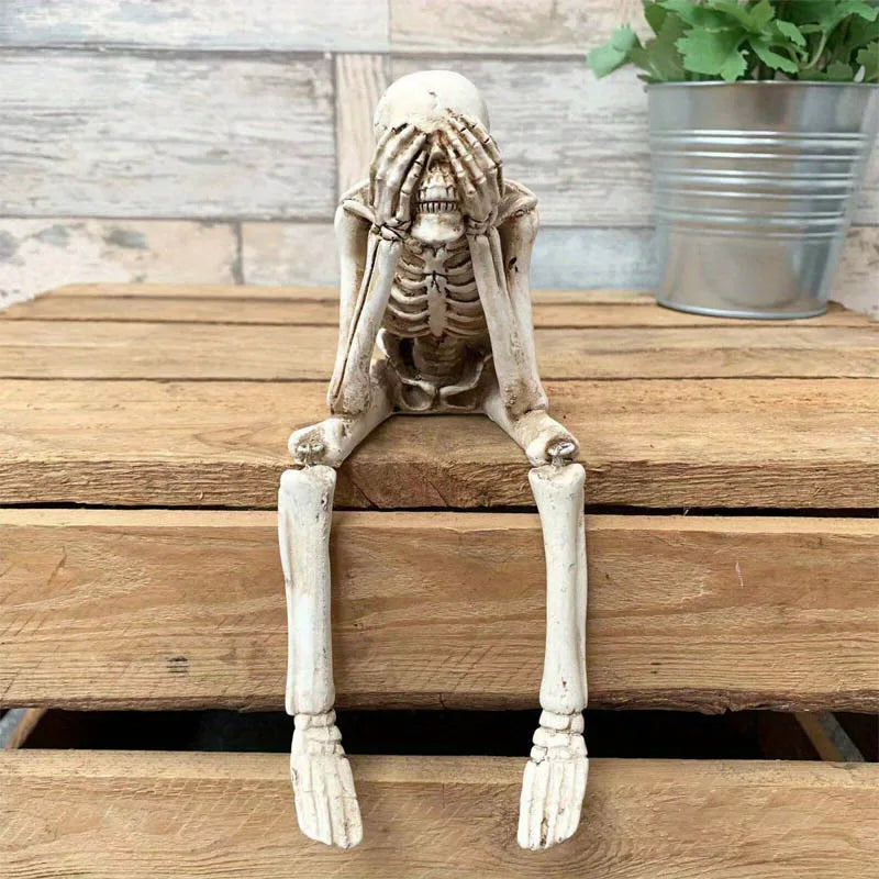 Skeletal figure with a sad expression sitting on a wooden surface.