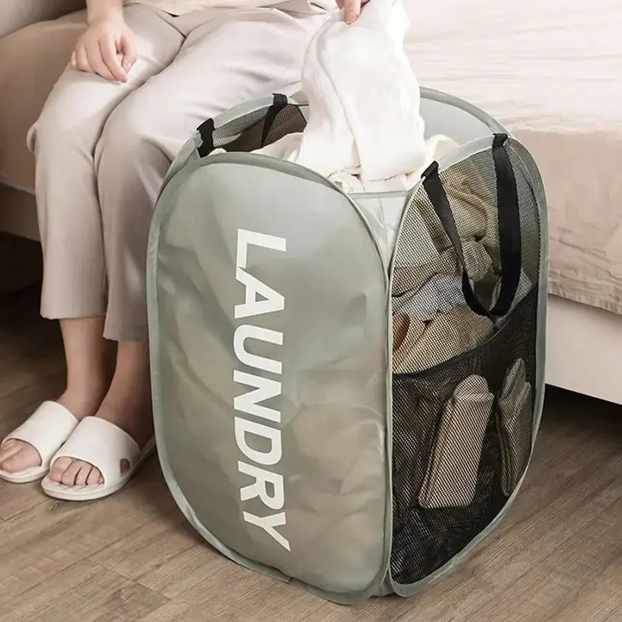 Person sitting on a couch with a laundry bag filled with clothes on the floor.