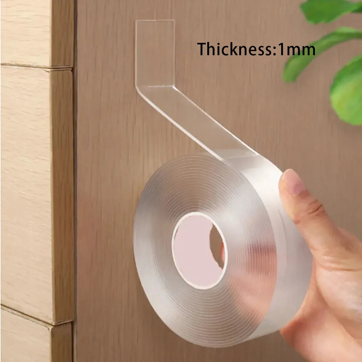 Hand holding a roll of clear tape with thickness indicated on a wooden surface.