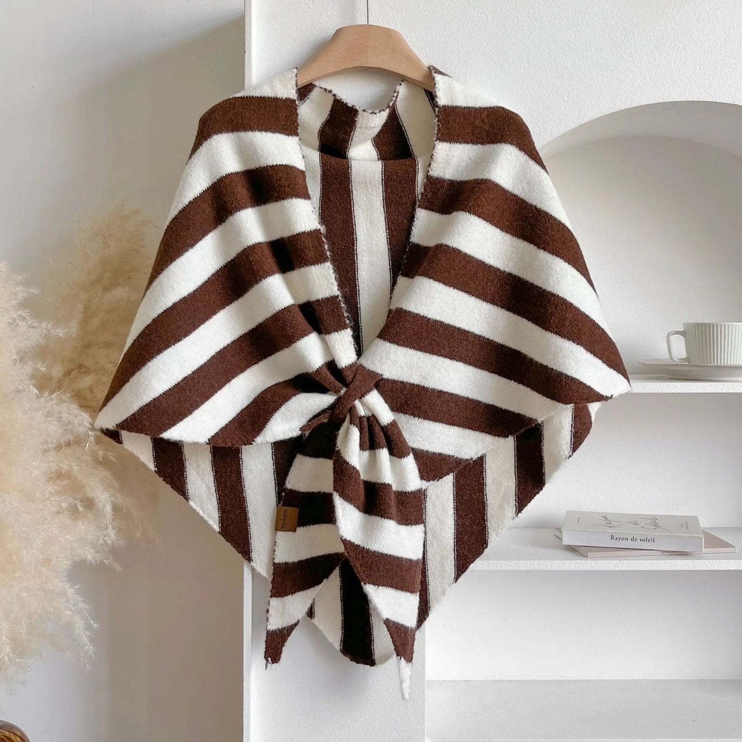 Brown and white striped poncho on a hanger against a neutral background