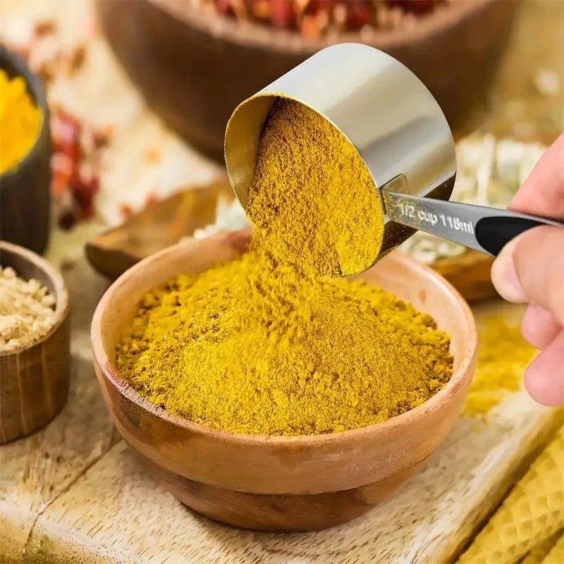 Yellow powder being poured from a measuring cup into a wooden bowl on a wooden surface.