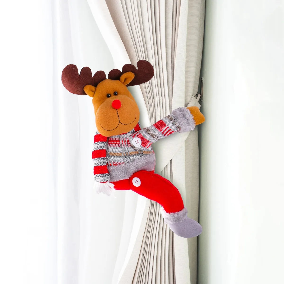 Plush reindeer curtain tieback with a striped sweater and red pants, hanging on a white curtain.