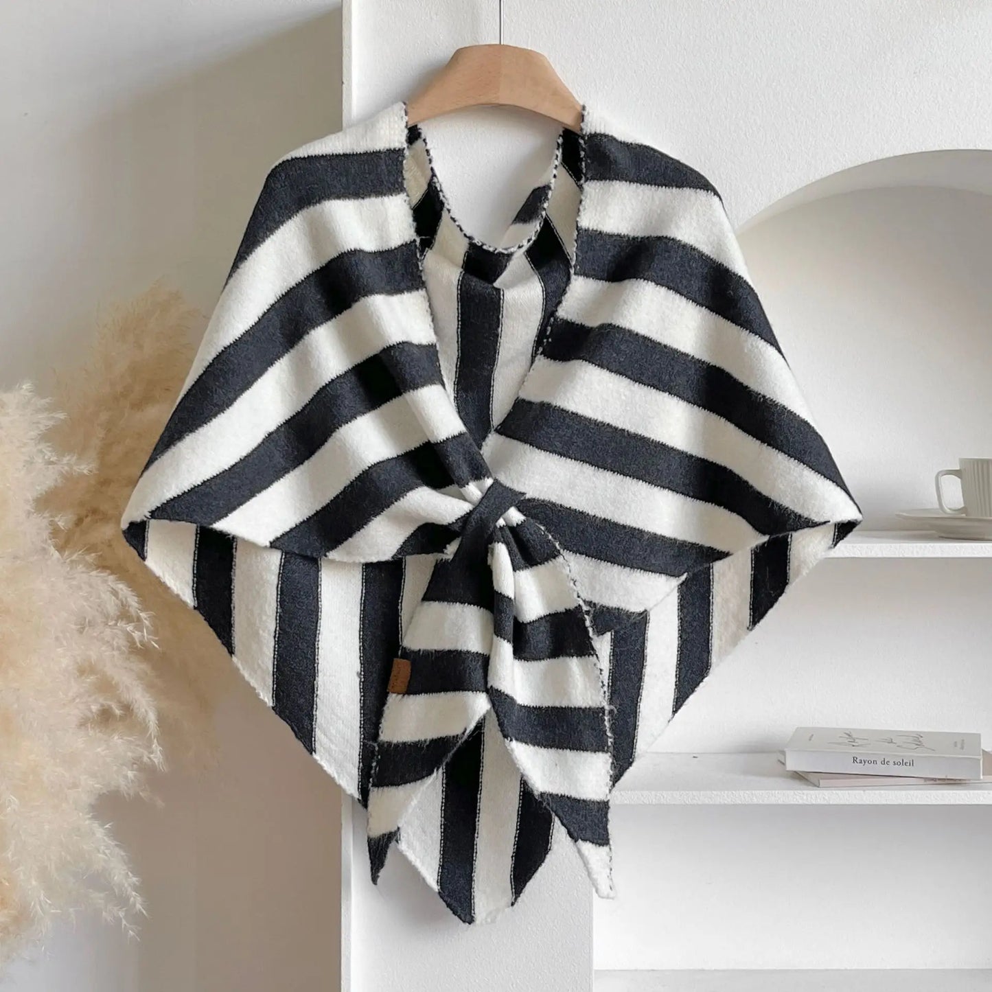 Black and white striped poncho on a wooden hanger against a neutral background