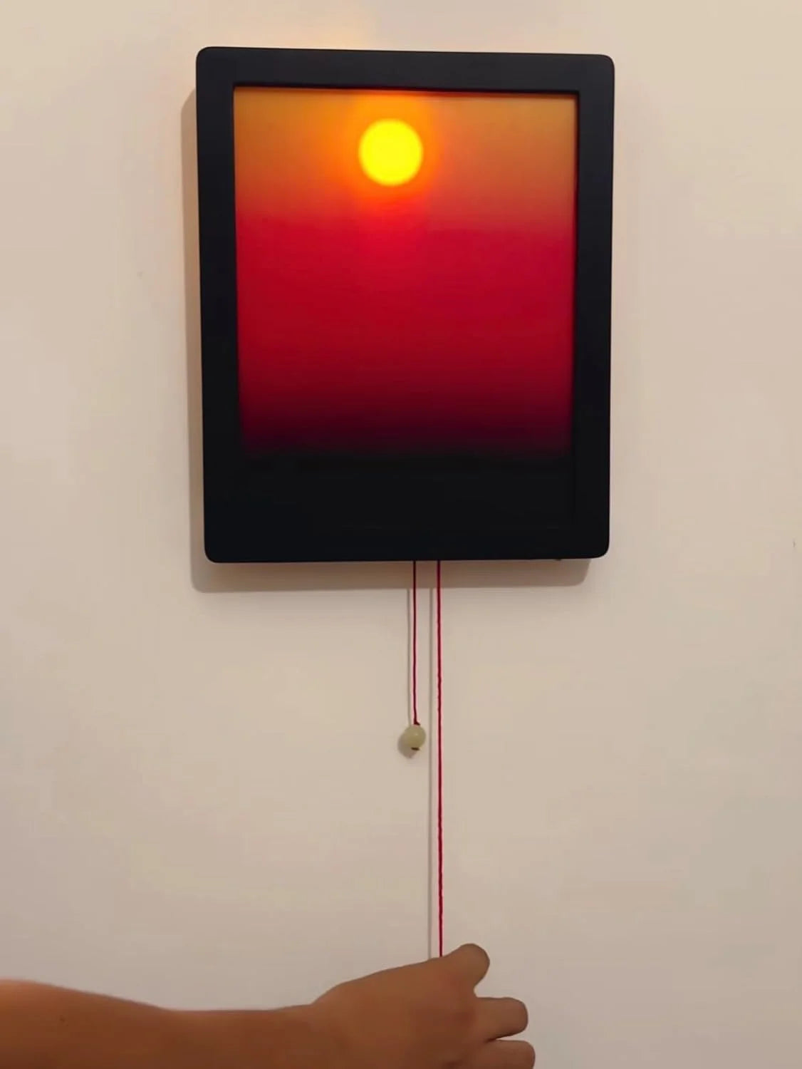 Rectangular light panel with a red glow on a white wall, controlled by a hand.