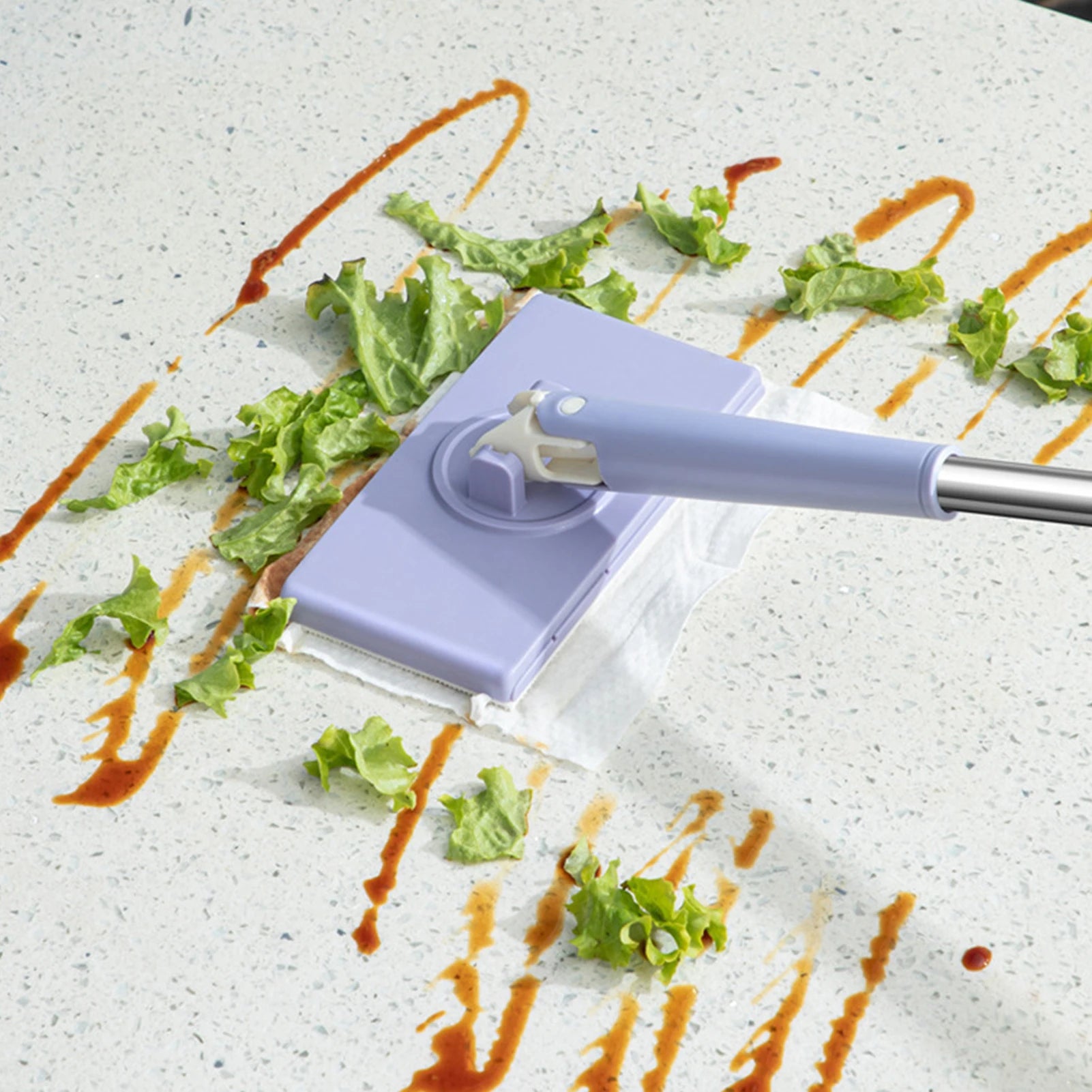 Cleaning tool with a purple handle and white head cleaning a surface with lettuce and sauce.