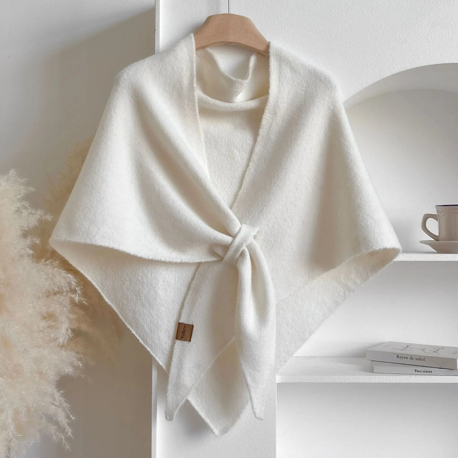 White poncho on a wooden hanger against a white wall with books and a mug in the background.