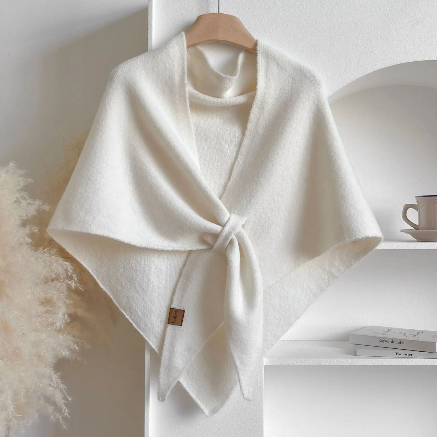 White poncho on a wooden hanger against a white wall with books and a mug in the background.
