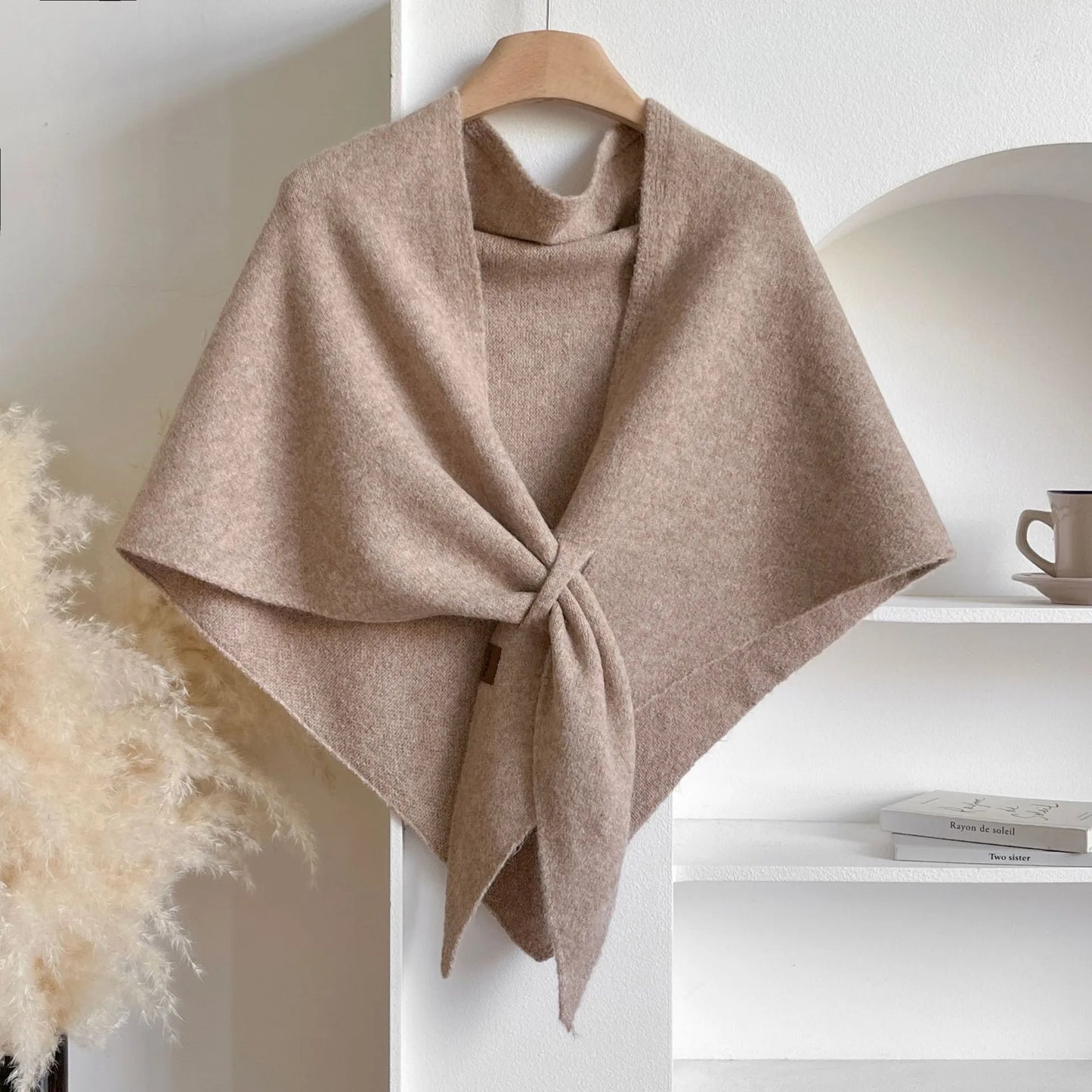 Beige poncho on a hanger against a neutral background