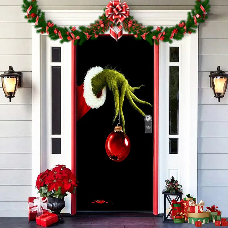 Decorative door with Grinch hand holding a red ornament, surrounded by Christmas decorations.