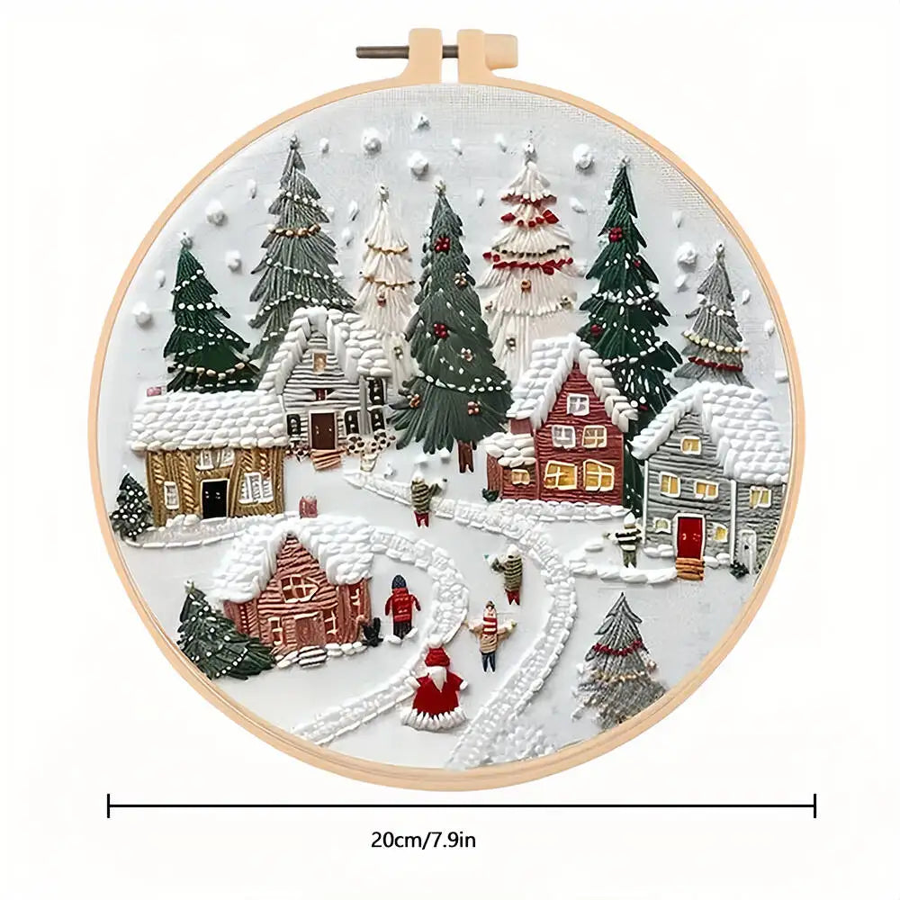 Embroidery hoop with a winter village scene, including houses, trees, and people, on a white background.