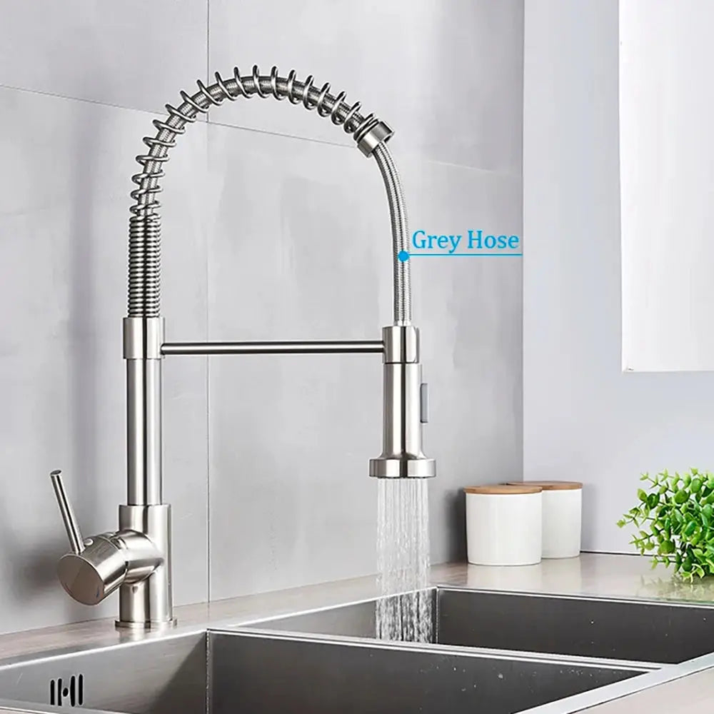 Modern kitchen faucet with water flowing into a sink against a light gray wall.