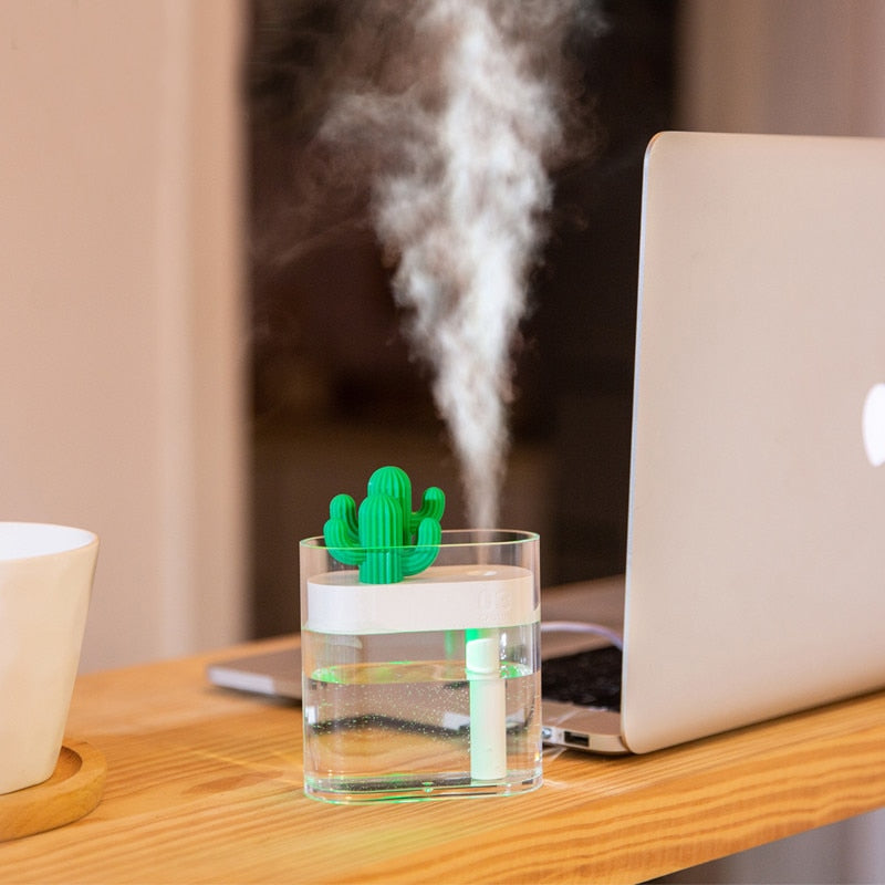 Cactus-shaped humidifier emitting steam on a desk with a laptop and cup in the background