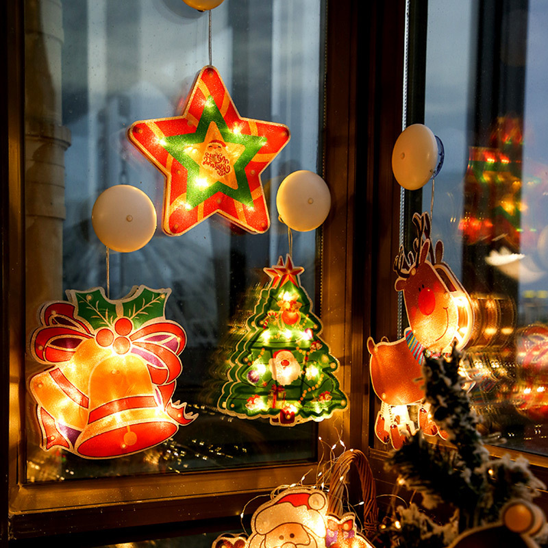 Decorative Christmas lights shaped like a star, bell, and tree hanging on a window.